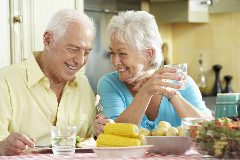 implant-supported-dentures-patients-eating-1 man and woman eating corn on the cob