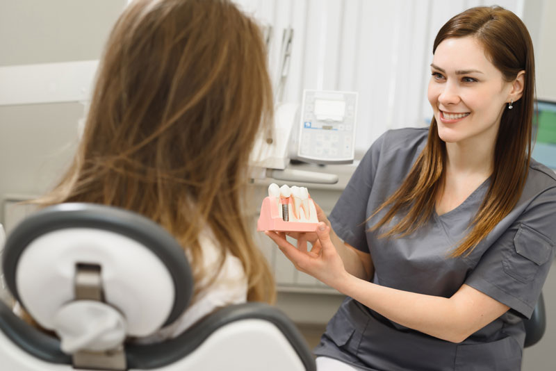 My Dental Company - Dental assistant showing a patient a dental implant model
